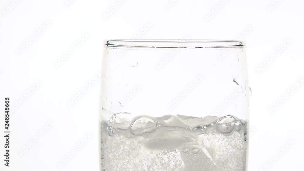 Close up dropping ice in glass of sparkling water Close up dropping ice in glass of sparkling water