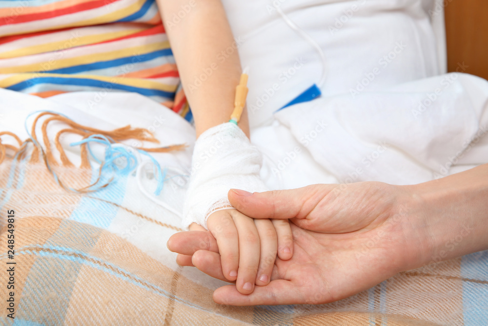 Fototapeta Doctor holding little child's hand with intravenous drip in hospital, closeup
