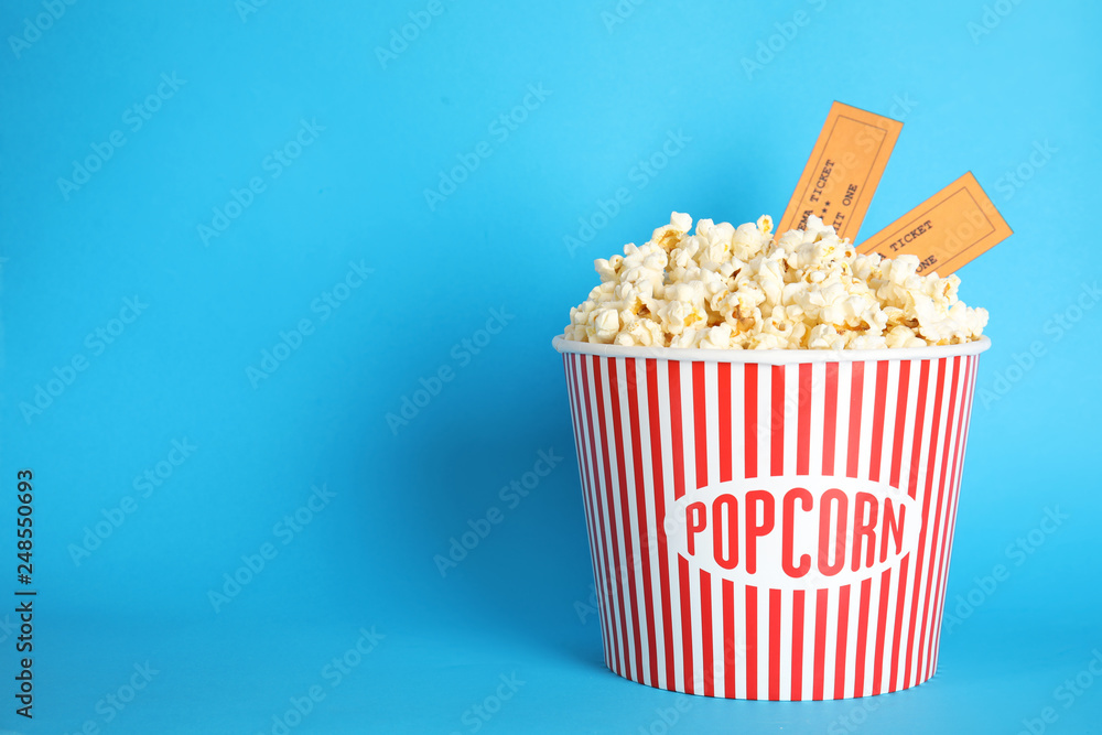 Bucket of fresh tasty popcorn and tickets on color background, space for text. Cinema snack