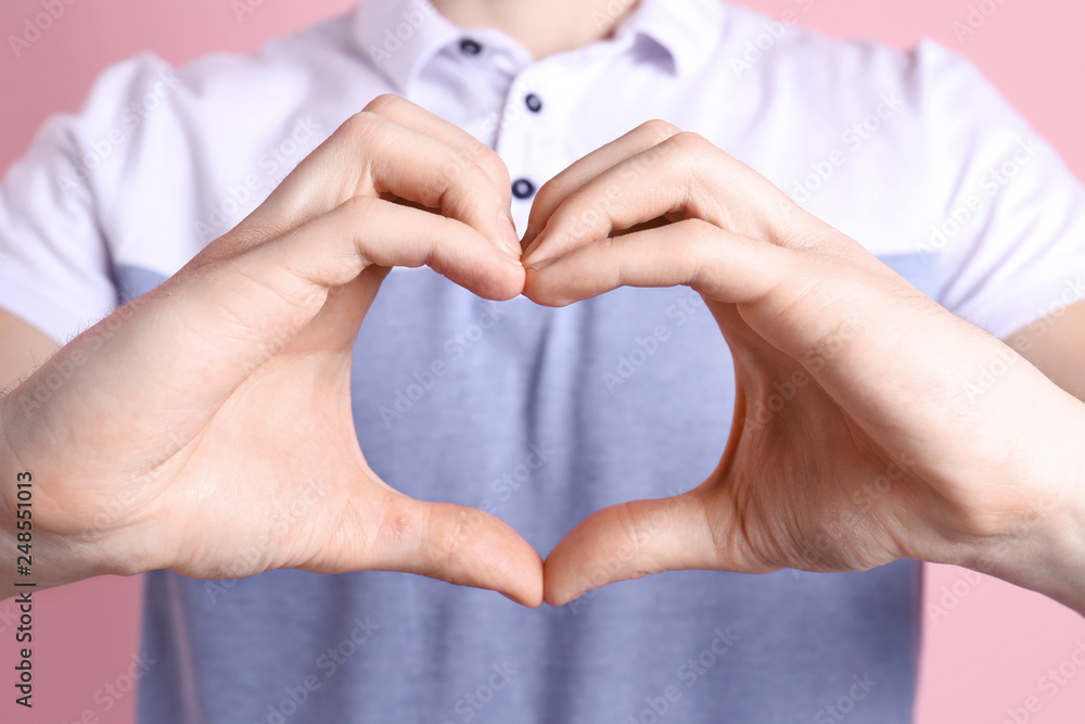 Fototapeta premium Young man making heart with his hands on color background, closeup