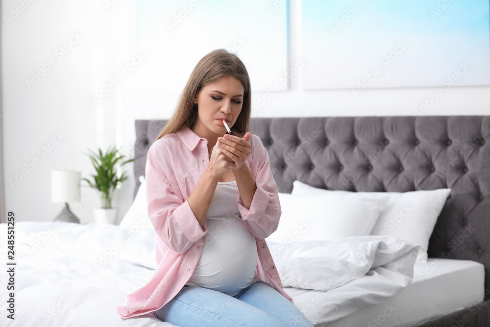 Young pregnant woman smoking cigarette in bedroom. Harm to unborn baby Young pregnant woman smoking cigarette in bedroom. Harm to unborn baby