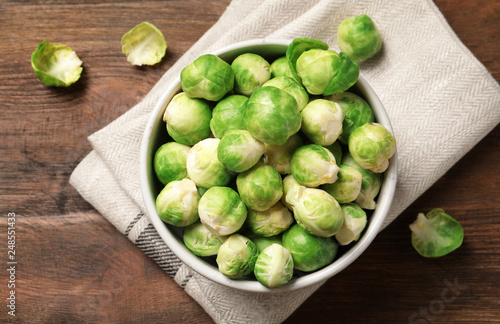 Bowl of fresh Brussels sprouts and napkin on wooden background, top view