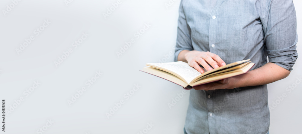 Junger Mensch mit grauem Hemd liest im geöffneten Buch als Banner Panorama - obrazy, fototapety, plakaty 