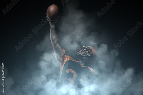 American football player on a dark background in smoke in black and orange equipment.