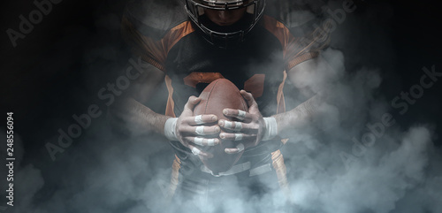 American football player on a dark background in smoke in black and orange equipment.