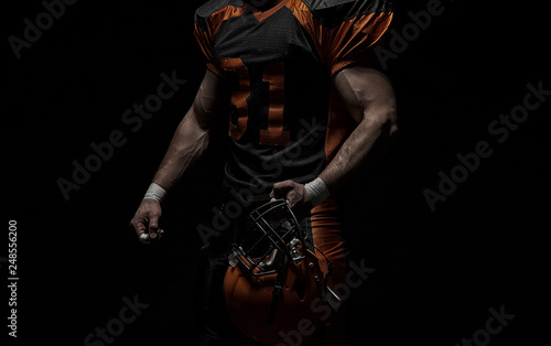 Fototapeta Naklejka Na Ścianę i Meble -  American football player on a dark background in black and orange equipment.