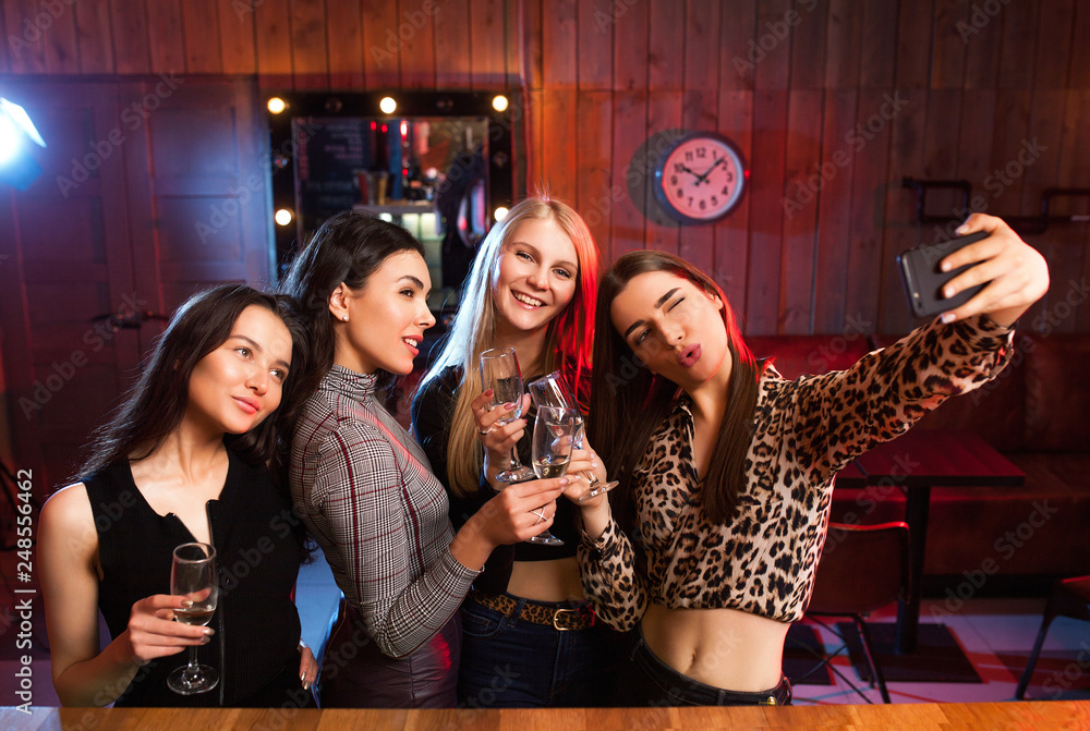Cheerful girls having fun by taking selfie and drinking cocktails in bar .