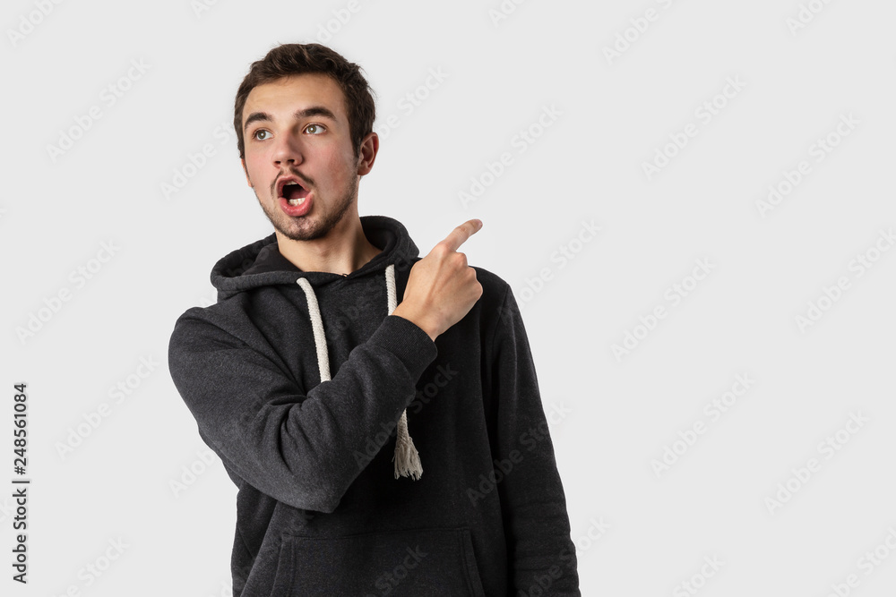 Amazed caucasian young man pointing backwards with shocked face. Isolated on white background. Advertisement concept. Amazed caucasian young man pointing backwards with shocked face. Isolated on white background. Advertisement concept.