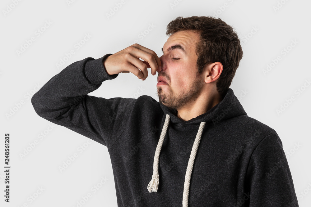 Disgusted caucasian young man holding his nose to avoid bad smell. Isolated on white background. Disgusted caucasian young man holding his nose to avoid bad smell. Isolated on white background.