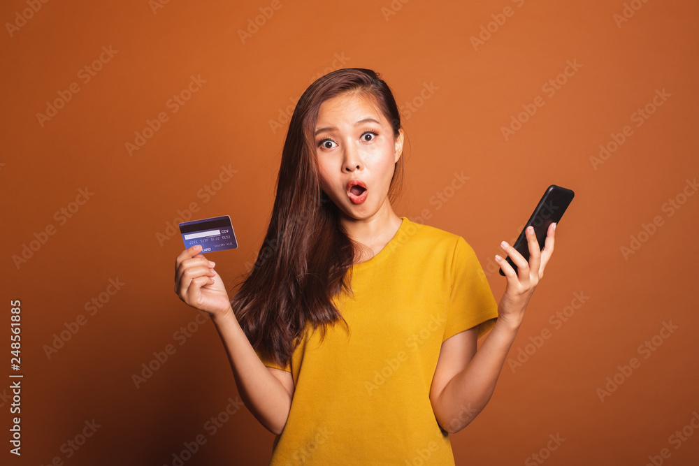 Young Asian woman using credit card and smart phone for online shopping, payment over orange background Young Asian woman using credit card and smart phone for online shopping, payment over orange background