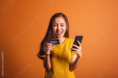 Young Asian woman using credit card and smart phone for online shopping, payment over orange background