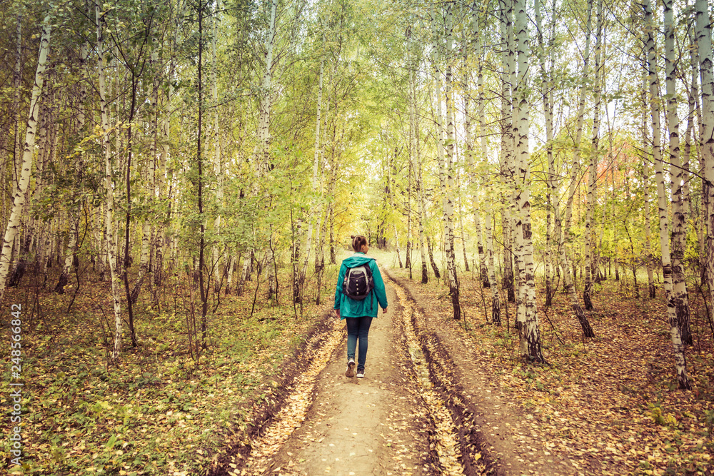 Girl with a backpack walks through the autumn forest