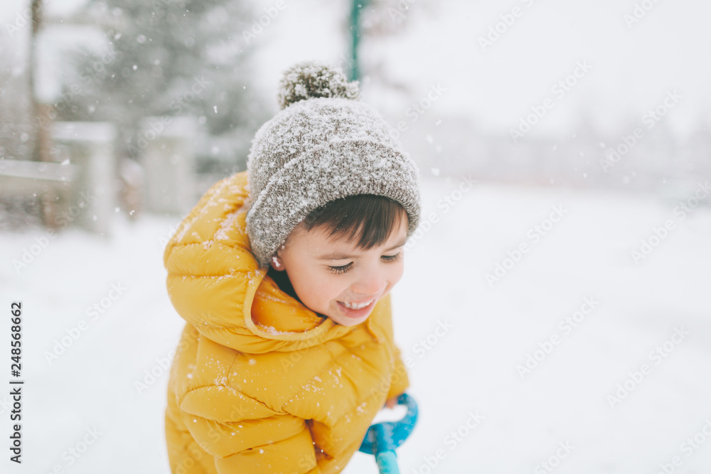 A happy little boy shovelling snow in winter. 