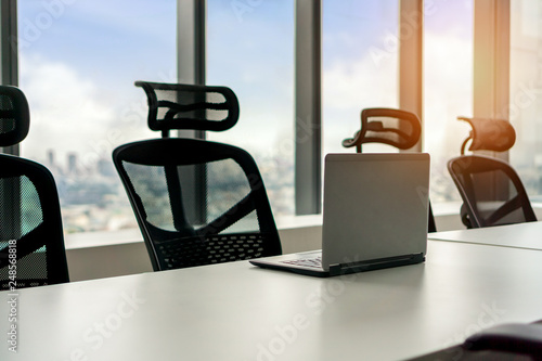 laptop on table in meeting room with large windows and city tower view with blur sky, Selective focus.
