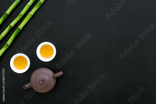 Asian tea traditions. Drink tea. Tea ceremony. Tea pot near cups of green tea and bamboo decoration on black background top view space for text