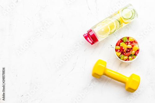 Healthy lifestyle, healthy habits. Detox water, fruit salad, sport equipment dumbbells on white stone background top view copy space
