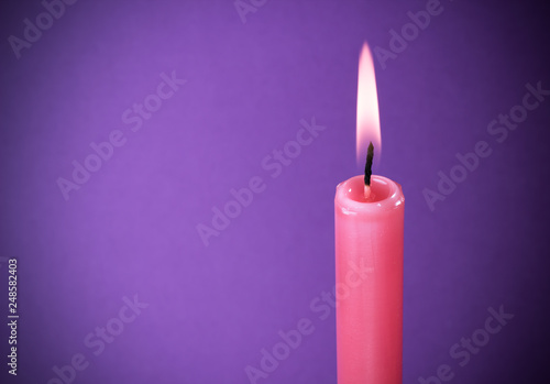 red burning candle on purple background