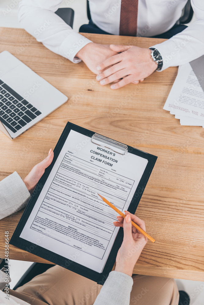 cropped view of businessman sitting at wooden desk while woman filling in compensation claim form cropped view of businessman sitting at wooden desk while woman filling in compensation claim form