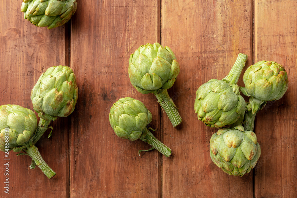 An overhead photo of many globe artichokes on a rustic wooden background with copy space An overhead photo of many globe artichokes on a rustic wooden background with copy space