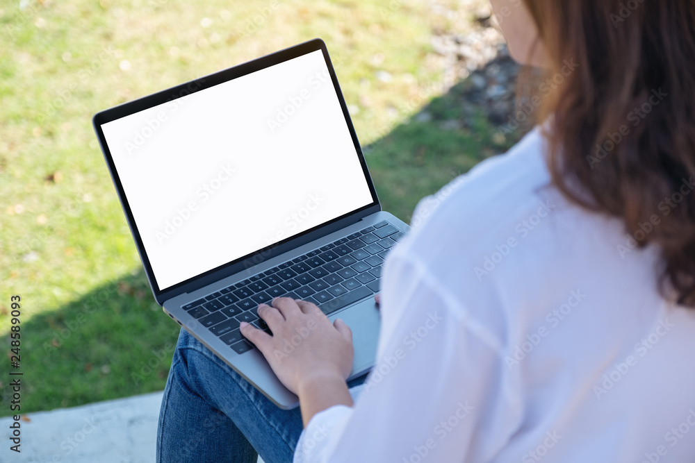 Mockup image of a woman using and typing on laptop with blank white screen , sitting in the outdoors with nature background Mockup image of a woman using and typing on laptop with blank white screen , sitting in the outdoors with nature background