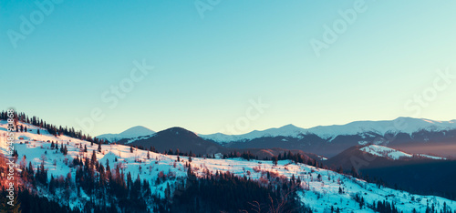 Beautiful winter panorama with fresh powder snow. Landscape with spruce trees, blue sky with sun light and colorful clouds and high mountains on background