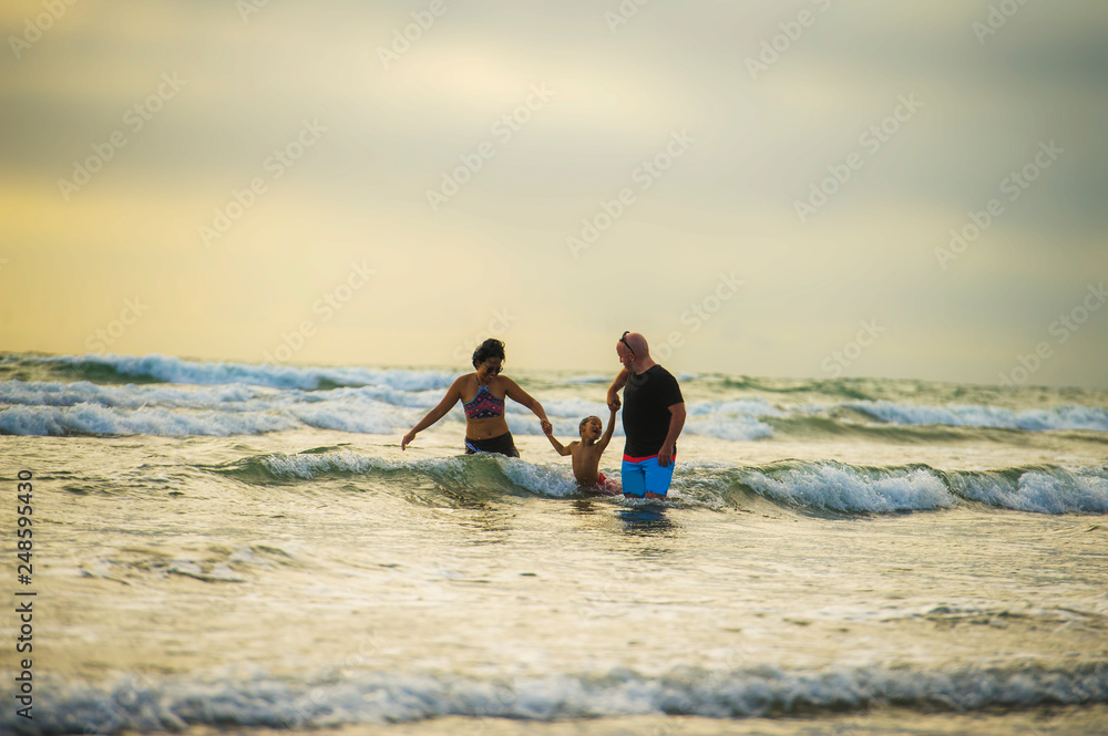 couple and little son walking relaxed on sunset beach enjoying romantic Summer holidays family trip the parents holding the child playing happy with waves and foam
