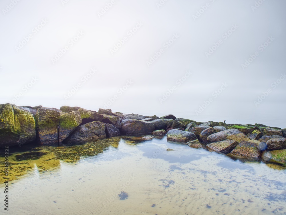 Fototapeta premium Stony coast defies to ocean clear sky with blurred Sun in high humidity.