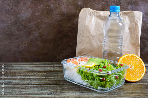Lunch box: rice salmon salad ottle of water on a wooden background. Fitness food. The concept of healthy eating. School lunch box. Copy space