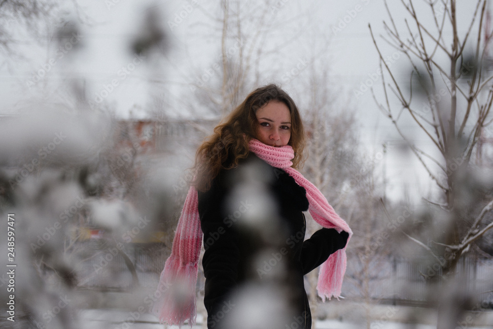 Young woman posing in a black coat and pink woolen scarf in the winter in the park Young woman posing in a black coat and pink woolen scarf in the winter in the park