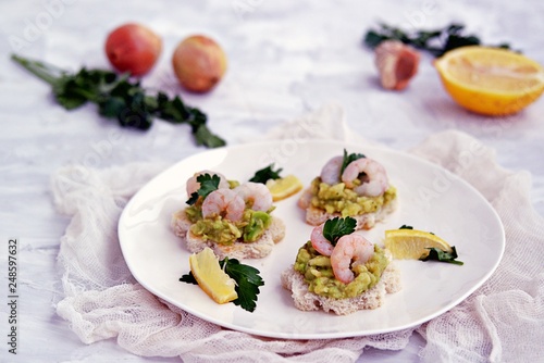 Small snack sandwiches on white bread with guacamole and shrimps on a white plate. Selective focus.