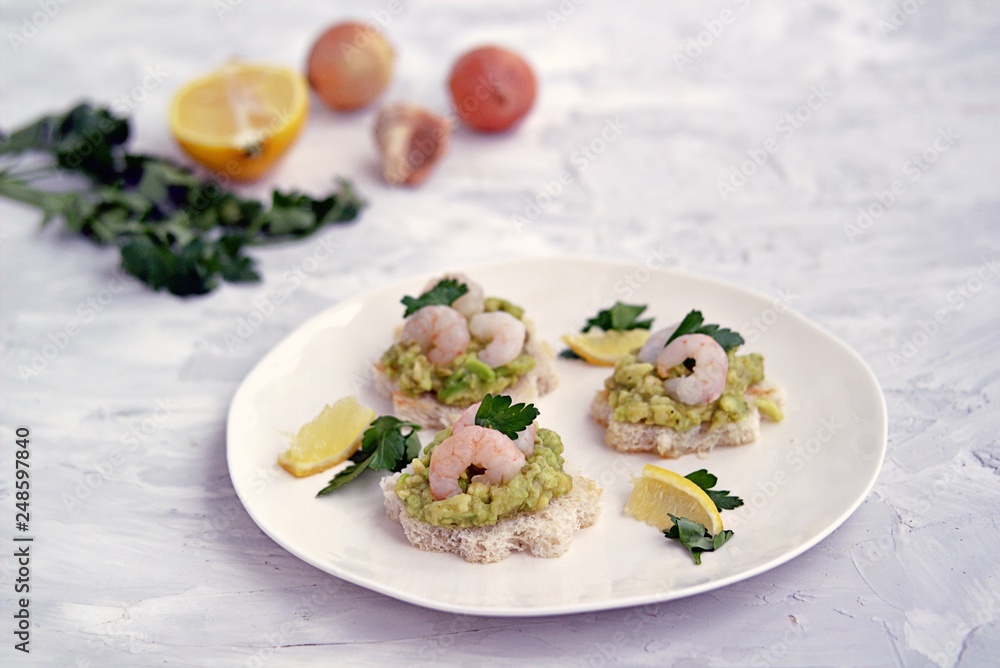 Small snack sandwiches on white bread with guacamole and shrimps on a white plate. Selective focus. Small snack sandwiches on white bread with guacamole and shrimps on a white plate. Selective focus.