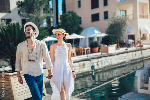 Foto Happy young couple walking by the harbor of a touristic sea resort with sailboat