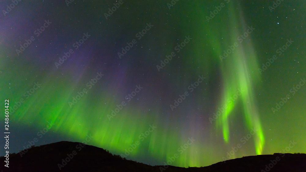 Northern, aurora borealis in the sky above the hills. Violet and green. Color.