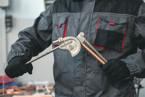 Fototapeta Pipe bender tool in a hands of factory worker on a factory workbench background