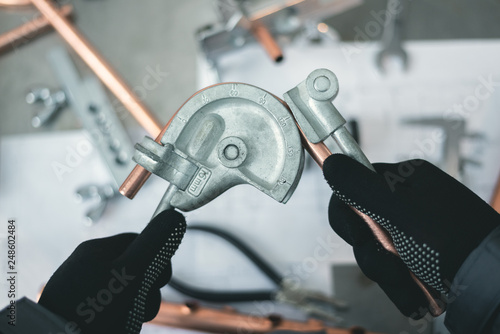 Pipe bender tool in a hands of factory worker on a factory workbench background. Fitter is bending a pipe. Pipework. photo