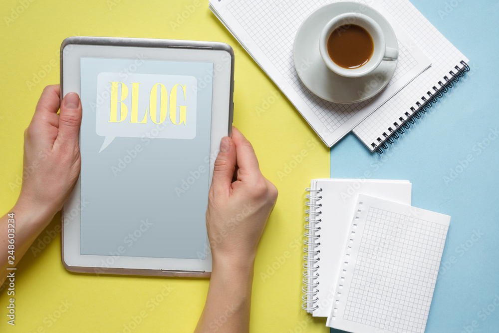Blogging, blog inscription on the tablet, cup of coffee, notebook on the desktop with a yellow and blue background, flat lay top view Blogging, blog inscription on the tablet, cup of coffee, notebook on the desktop with a yellow and blue background, flat lay top view