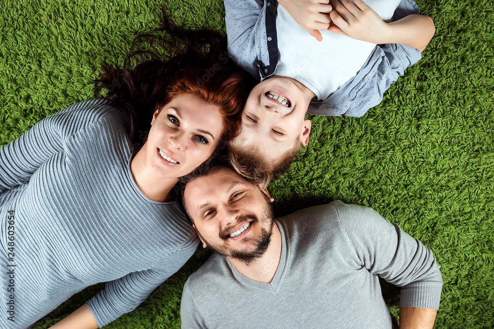 Top view, happy family, dad mom and son are smiling lying on a green carpet. The concept of family, family relationships, happiness, joy. Top view, happy family, dad mom and son are smiling lying on a green carpet. The concept of family, family relationships, happiness, joy.