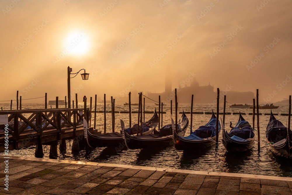 Gondolas in Venice at sunrise with Saint Giorgio island in morning fog, as seen from San Marco square