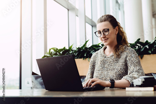 Happy caucasian woman millennial using laptop while sitting at cafe. Young businesswoman sitting in coffee shop, working on computer. Online marketing, business education for adult, teleworking.