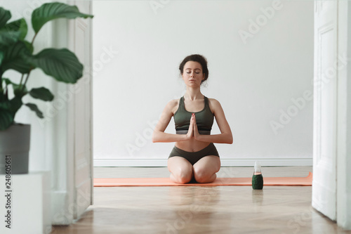 Young active, dark hair woman exercising and stratching her body on the floor at her studio. Girl is practicing yoga and thinking about positive things. Healthy lifestyle and mental balance. 