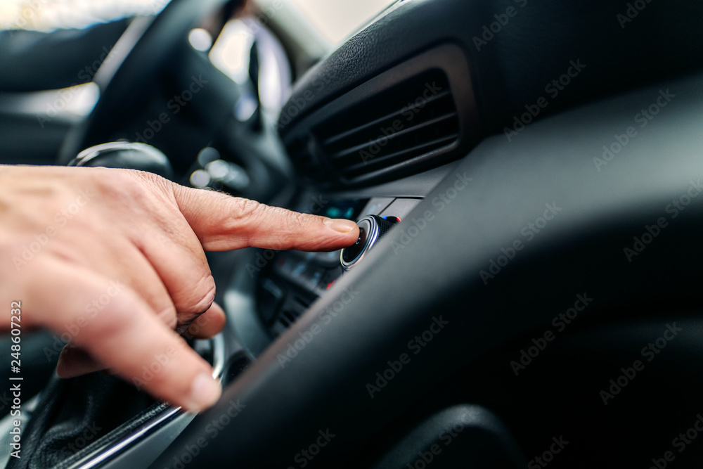 Close up of man searching good radio station while sitting in car.