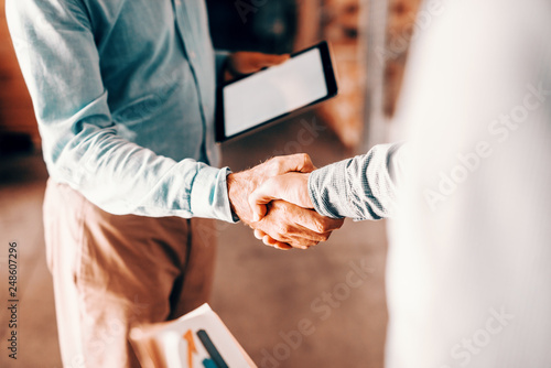 Close up of two modern businessman shaking hands for good negotiations and standing in warehouse.