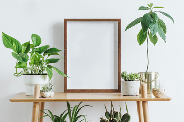 Scandinavian room interior with mock up photo frame on the brown bamboo shelf with beautiful plants in differents hipster and design pots. White walls. Modern and floral concept of shelfs.