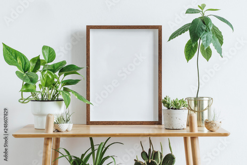 Scandinavian room interior with mock up photo frame on the brown bamboo shelf with beautiful plants in differents hipster and design pots. White walls. Modern and floral concept of shelfs. photo