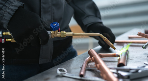 Bild auf Leinwand Worker is soldering a pipe by a blow lamp on a factory workbench background