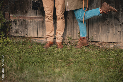 Man and woman standing near wooden rural house. closeup shoes. Stylish couple feet, in love, their legs