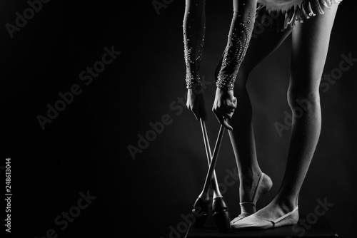 Teenager girl gymnast holds in hands clubs for rhythmic gymnastics.near the legs photo