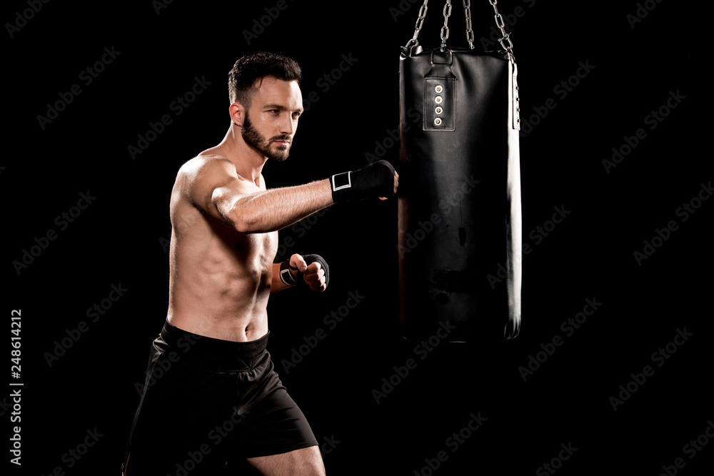 muscular boxer hitting punching bag isolated on black