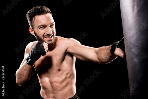 shortless sportsman kicking punching bag isolated on black © LIGHTFIELD STUDIOS