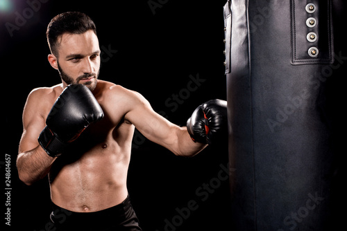 bearded sportsman wearing boxing gloves hitting punching bag isolated on black